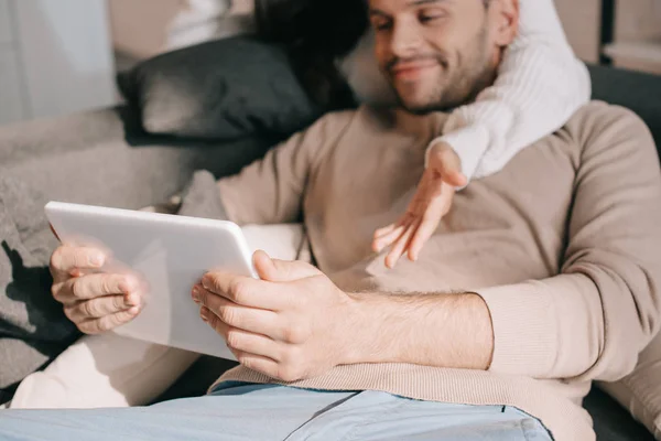 Corte tiro de jovem casal usando tablet juntos no sofá em casa — Fotografia de Stock