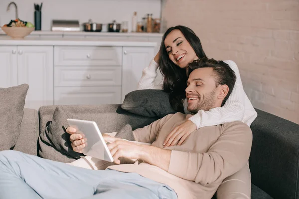 Riendo joven pareja usando tableta juntos en sofá en casa - foto de stock