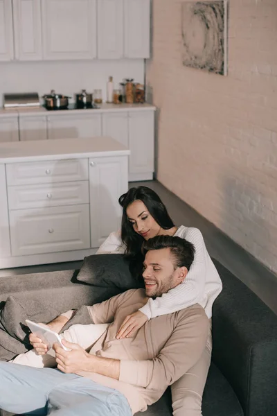 Vista ad alto angolo di sorridere giovane coppia utilizzando tablet insieme sul divano di casa — Foto stock