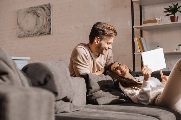 Feliz joven pareja usando tableta juntos en sofá en casa - foto de stock