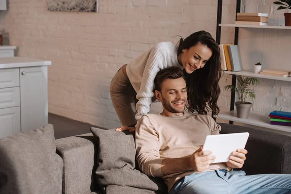 Belo jovem casal usando tablet juntos no sofá em casa — Fotografia de Stock
