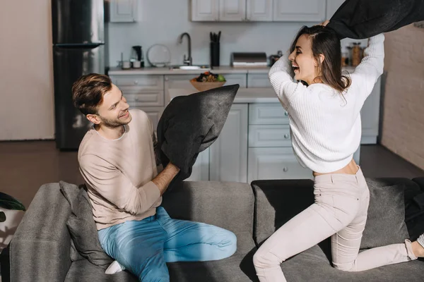 Belo jovem casal lutando com travesseiros no sofá em casa — Fotografia de Stock