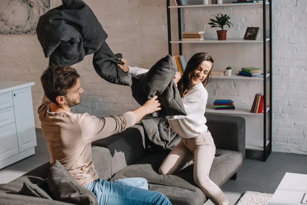 Lachendes junges Paar kämpft mit Kissen auf der heimischen Couch — Stockfoto