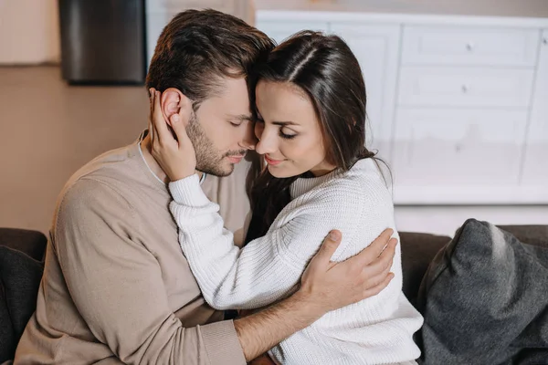 Belo jovem casal abraçando no sofá em casa — Fotografia de Stock