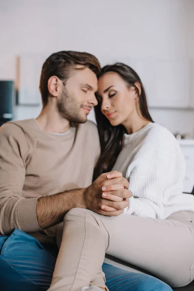 Happy young couple cuddling and holding hands on couch at home — Stock Photo