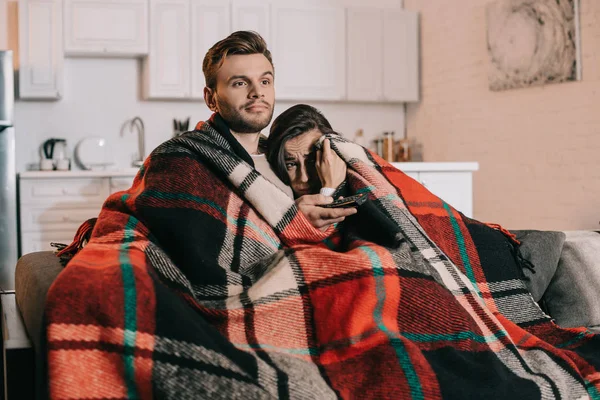 Jeune couple se détendre sur le canapé et regarder la télévision ensemble tout en couvrant avec plaid — Photo de stock