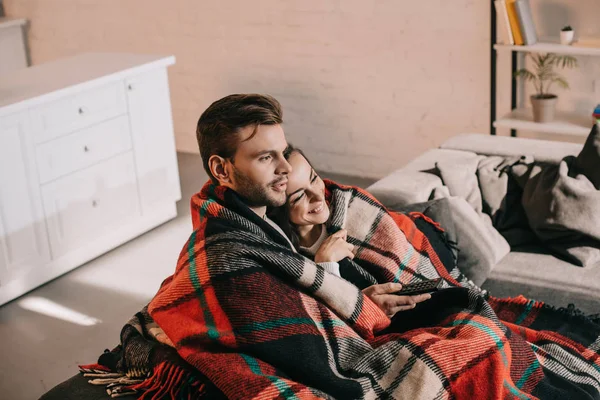 Schönes junges Paar, das es sich auf der Couch gemütlich macht und gemeinsam fernsieht, während es sich mit Plaid bedeckt — Stockfoto