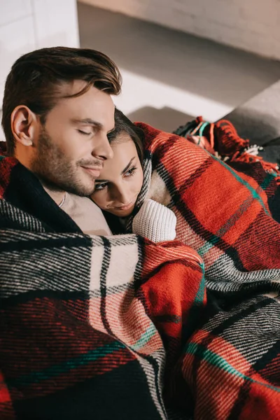 High angle view of happy young couple relaxing on couch and covering with plaid — Stock Photo