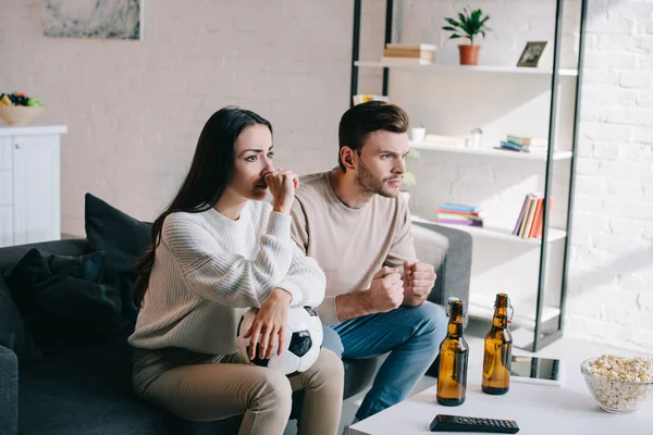 Seria joven pareja viendo fútbol partido en sofá en casa - foto de stock
