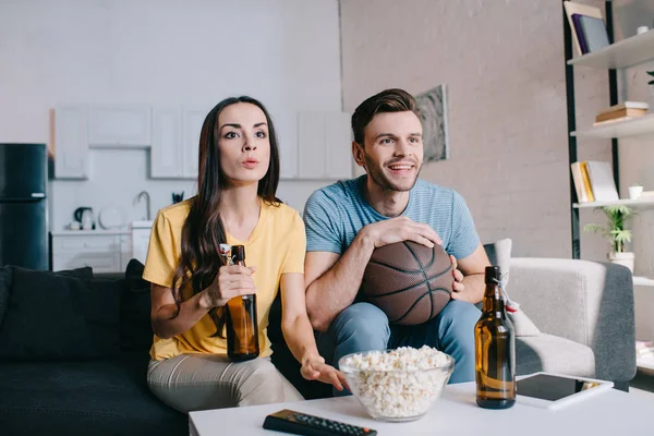 Happy young couple watching basketball game on tv at home — Stock Photo