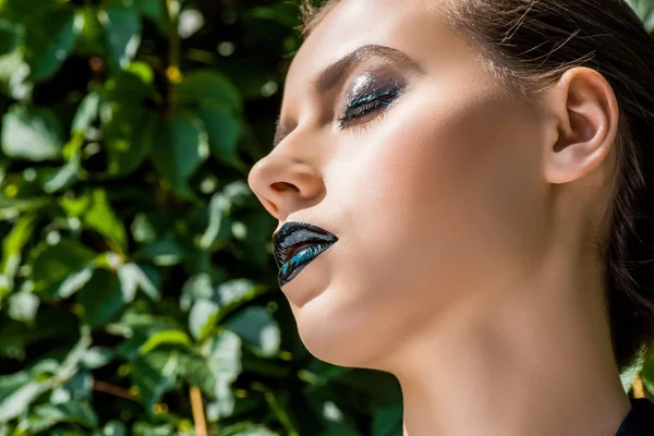 Jeune femme aux lèvres noires et aux feuilles vertes à l'arrière-plan — Photo de stock