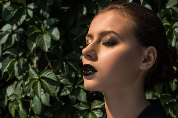 Young woman with closed eyes and green leaves at background — Stock Photo