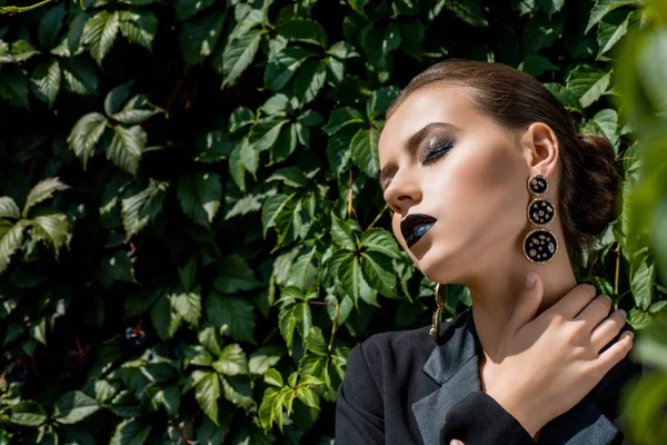 Hermosa mujer joven con rayos de sol en la cara y hojas verdes en el fondo - foto de stock