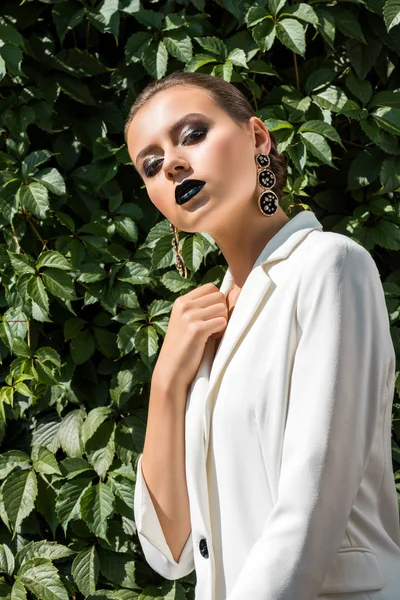 Mujer joven con estilo en chaqueta blanca con hojas verdes en el fondo — Stock Photo