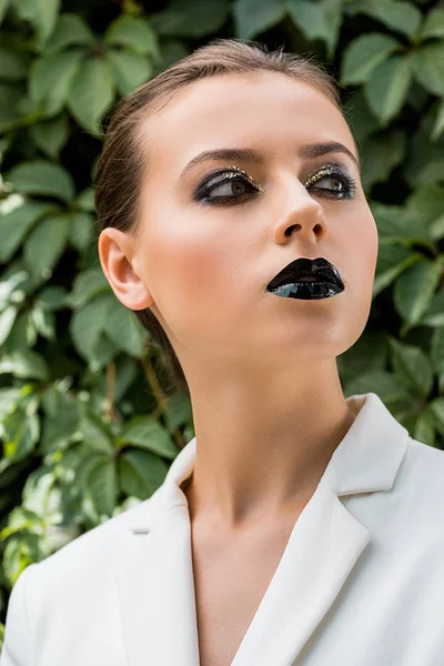 Mujer joven con estilo en chaqueta blanca con hojas verdes en el fondo - foto de stock