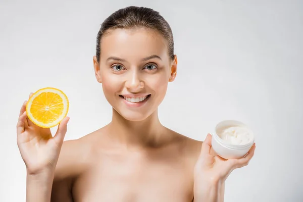 Giovane bella donna in possesso di crema corpo bianco e fetta arancione — Foto stock