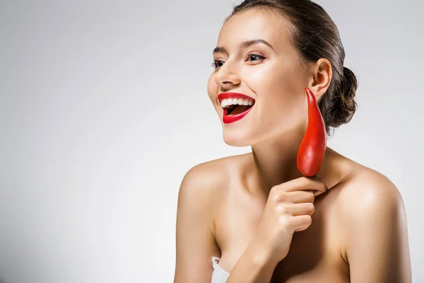 Joven sonriente hermosa mujer con labios rojos sosteniendo chile cerca de la cara — Stock Photo
