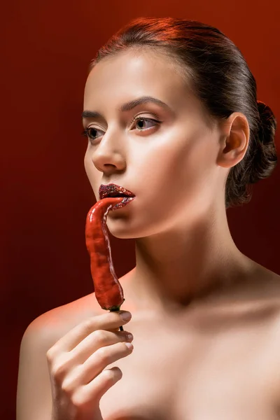 Mujer atractiva joven con labios brillantes y chile rojo sobre fondo borgoña - foto de stock