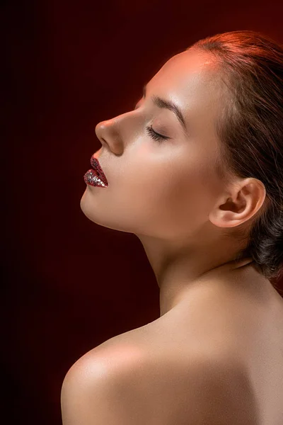 Молода жінка з блискучими губами і закритими очима на бордовий фон — стокове фото