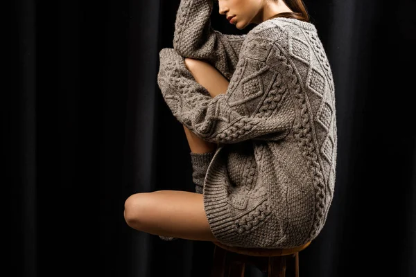 Teilweise sieht man eine Frau in grauem Wollpullover auf einem Barhocker vor schwarzem Hintergrund sitzen. — Stockfoto