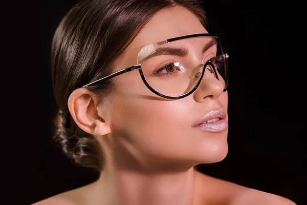 Portrait of beautiful woman in fashionable eyeglasses with bare shoulders looking away isolated on black — Stock Photo