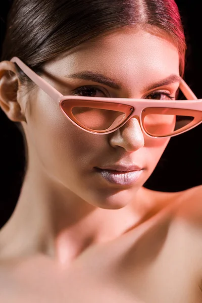 Retrato de modelo hermoso en gafas de moda mirando a la cámara aislada en negro - foto de stock