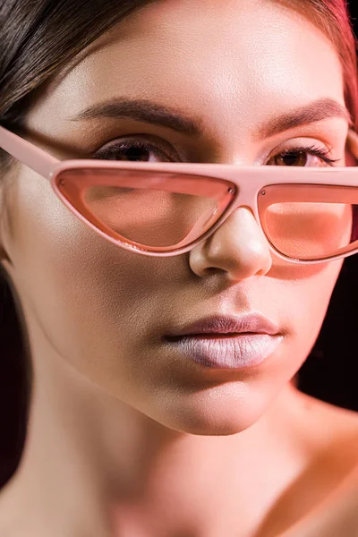 Retrato de modelo hermoso en gafas de moda mirando a la cámara aislada en negro - foto de stock