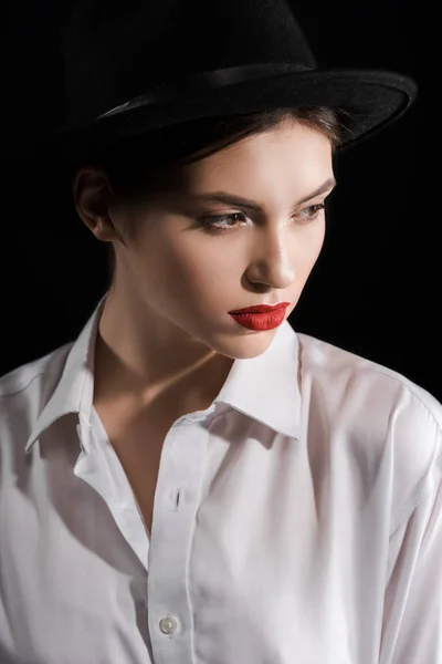 Portrait of fashionable model in white shirt and black hat isolated on black — Stock Photo