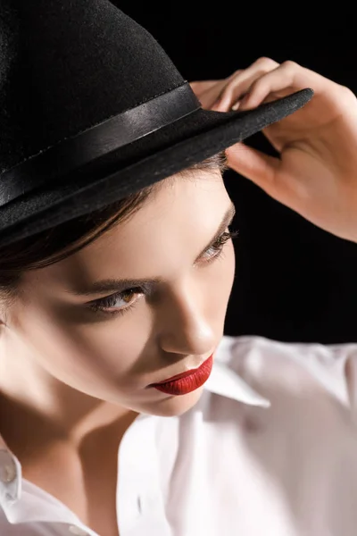 Elegante modelo pensativo com lábios vermelhos na camisa branca e chapéu preto posando isolado no preto — Fotografia de Stock