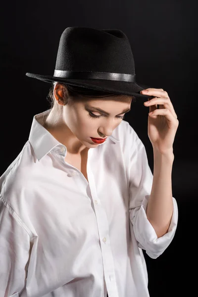 Modelo jovem elegante com lábios vermelhos na camisa branca e chapéu preto posando isolado no preto — Fotografia de Stock