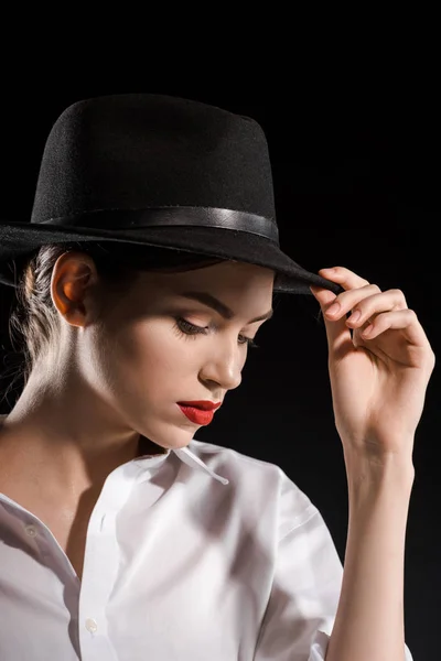 Portrait of beautiful woman in white shirt and black hat posing isolated on black — Stock Photo