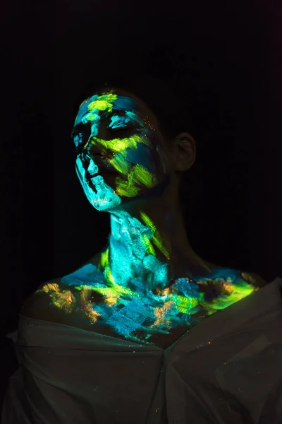 Femme avec des peintures ultraviolettes sur le visage posant sur fond noir — Photo de stock