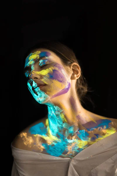 Mujer con pinturas ultravioletas en la cara posando sobre fondo negro - foto de stock