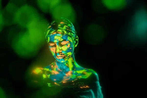 Portrait of woman painted with bright neon paints on black backdrop with bokeh lights — Stock Photo