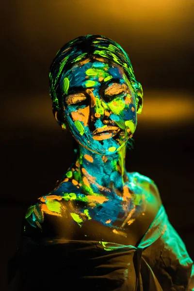 Portrait of woman painted with bright neon paints on dark backdrop — Stock Photo