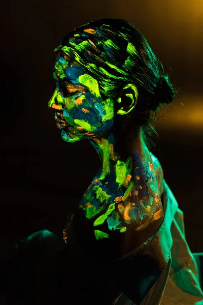 Вид збоку жінки, намальованої барвистими ультрафіолетовими фарбами на чорному тлі — стокове фото