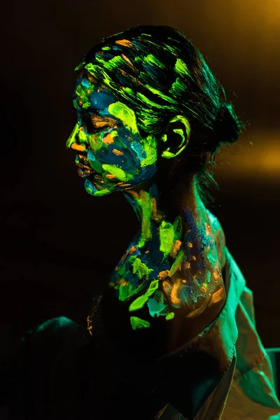 Side view of woman painted with colorful ultraviolet paints on black backdrop — Stock Photo