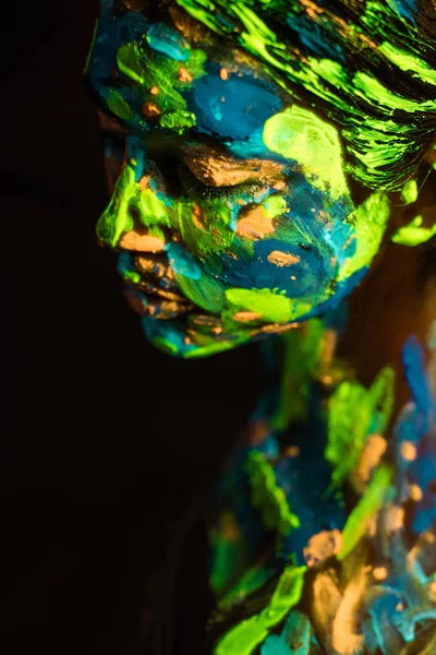 Side view of woman painted with colorful ultraviolet paints on black backdrop — Stock Photo