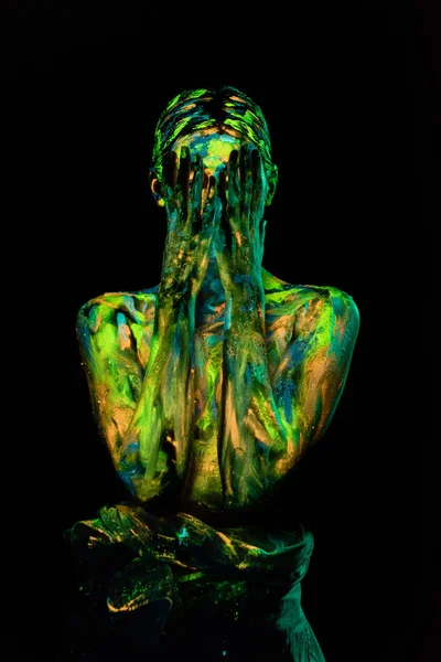 Visão obscurecida da mulher pintada com tintas ultravioletas cobrindo o rosto no fundo preto — Fotografia de Stock