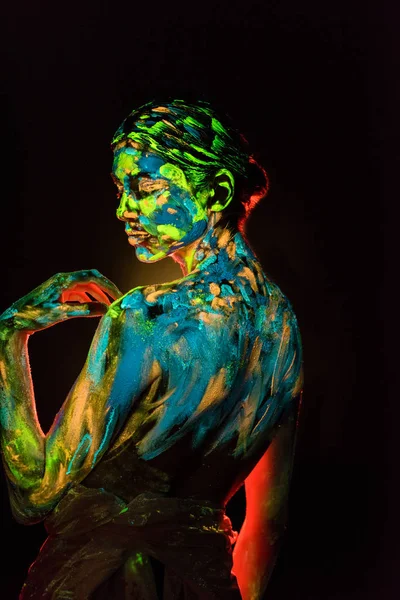 Vue latérale de la femme peinte avec des peintures ultraviolettes colorées sur fond noir — Photo de stock