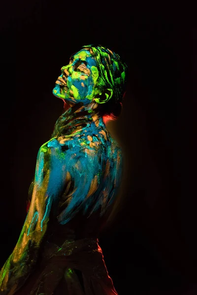 Side view of woman painted with colorful ultraviolet paints on black backdrop — Stock Photo