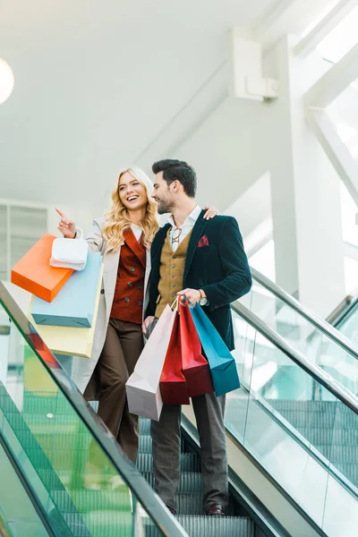 Beautiful couple with shopping bags standing on escalator — Stock Photo