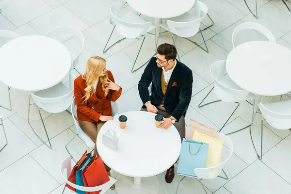 Overhead view of stylish couple of shopaholics with shopping bags and coffee to go sitting in cafe — Stock Photo
