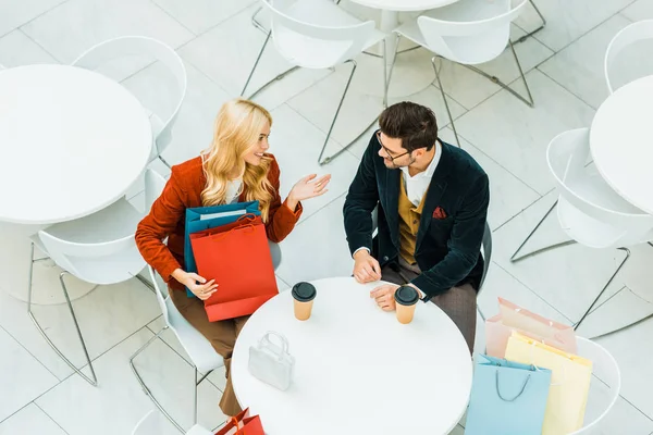 Overhead view of beautiful happy couple with shopping bags talking and sitting in cafe — Stock Photo
