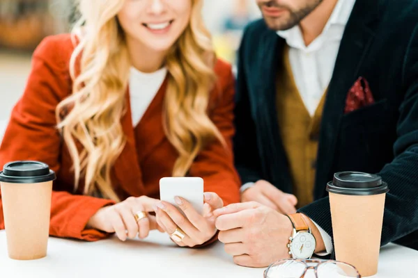 Vista ritagliata di coppia utilizzando smartphone in caffè con caffè da andare — Foto stock