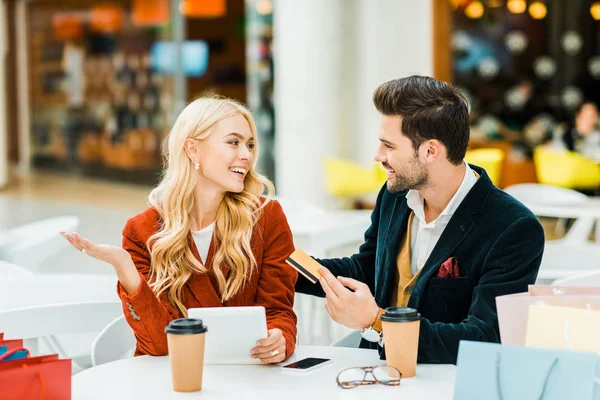 Happy stylish couple shopping online with credit card and tablet while sitting in cafe in shopping center — Stock Photo