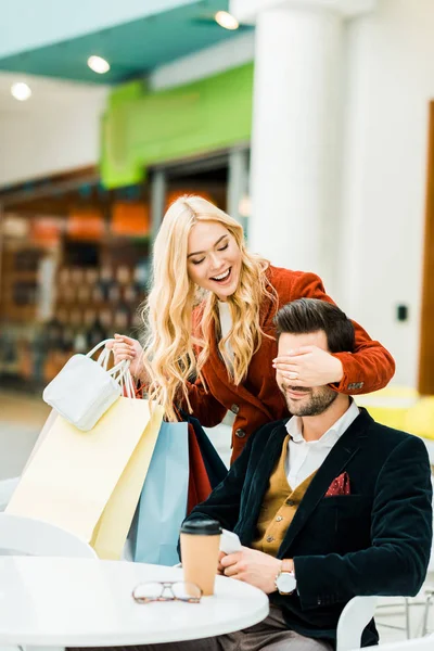 Aufgeregtes modisches Mädchen mit Einkaufstüten, die Augen schließen und für Freund eine Überraschung machen — Stockfoto