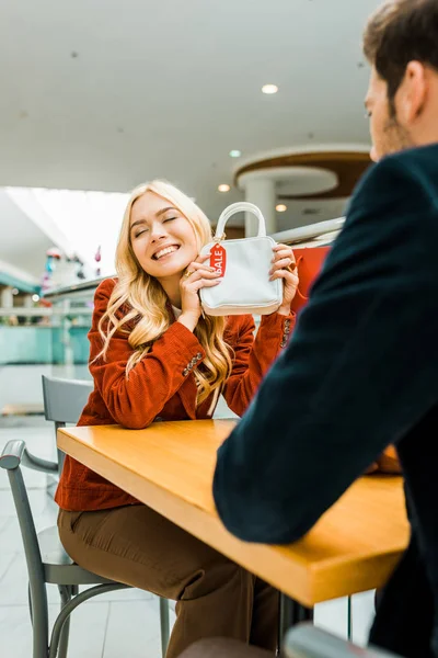 Felice donna attraente che mostra borsa con tag vendita al fidanzato nel centro commerciale — Foto stock