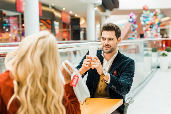 Stylish man taking photo of girlfriend holding bag with sale tag — Stock Photo