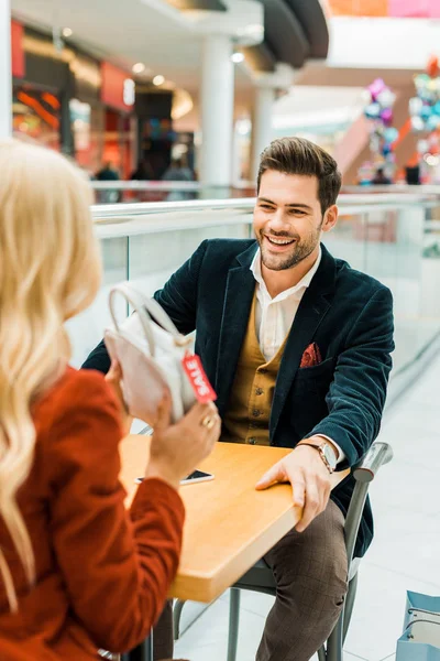 Blonde woman showing bag with sale tag to man — Stock Photo